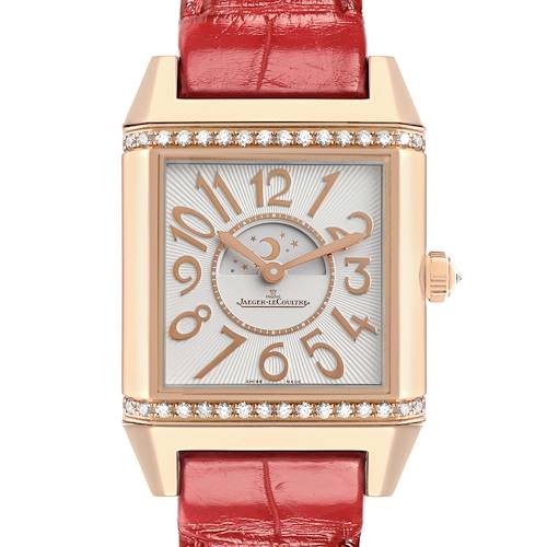 The Reverso watch by Jaeger LeCoultre is shown from a front angle, highlighting the dial, red strap, and diamond-set bezel.